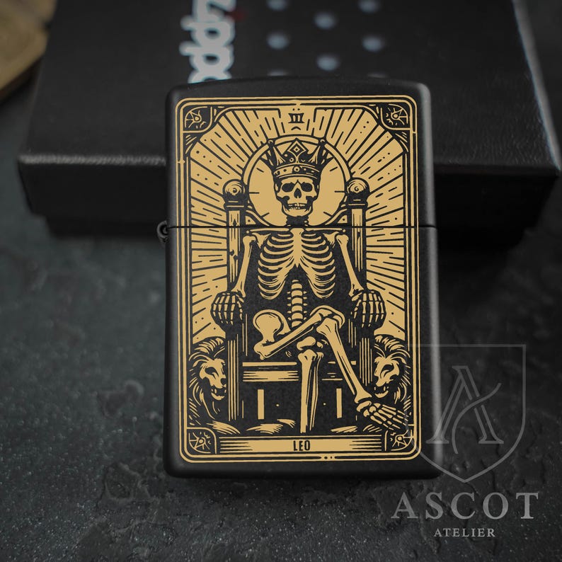 May include: A matte black metal lighter featuring a gold-colored engraved design of a skeleton wearing a crown and sitting on a throne flanked by two lions. The design includes the text LEO at the bottom and Roman numeral III at the top.