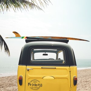 May include: A yellow vintage van with a surfboard on top. The van has a black roof and a sticker on the back that says "Little Princess on board".