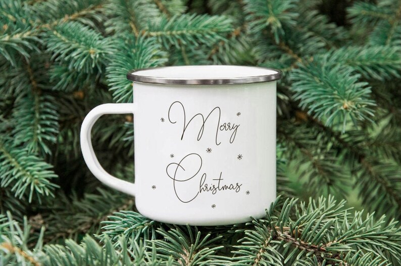 Puede incluir: Taza de esmalte blanco con una inscripci&oacute;n negra que dice "Feliz Navidad" rodeada de peque&ntilde;os dise&ntilde;os de copos de nieve.