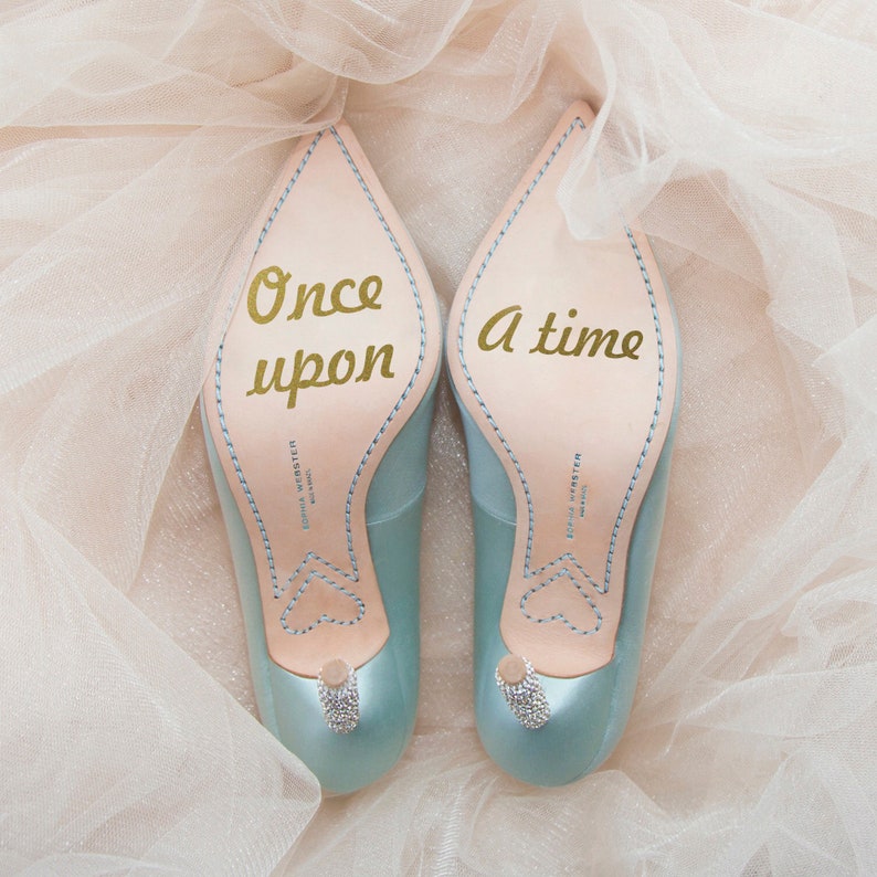 May include: A pair of light blue satin heels with a gold inscription on the soles. The left shoe says "Once upon" and the right shoe says "a time".