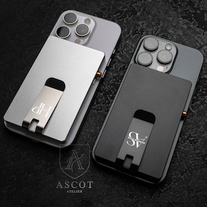 May include: Two phone cases with attached cardholders. One is silver, the other black. Each has a metal stand with a logo. The silver case has the letters "JII" and "LID" on the stand. The black case has "SV" and "ANDREW STAR" on the stand.