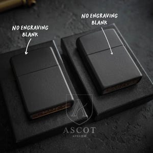 May include: Two matte black metal lighters with a rectangular shape and a hinged lid. Each lighter is positioned on a black box. Text on the image points to each lighter with the label NO ENGRAVING BLANK. The brand name ASCOT ATELIER is visible.