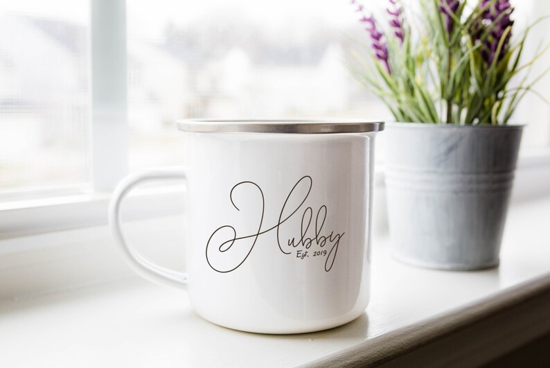 Puede incluir: Taza de esmalte blanco con una inscripci&oacute;n cursiva negra que dice "Hubby Est. 2019".