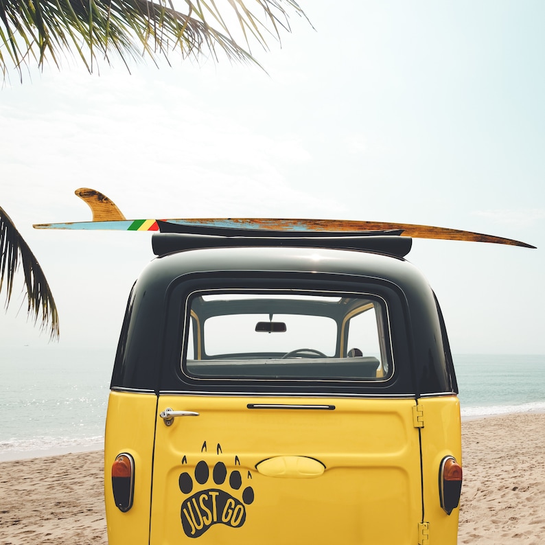 May include: A yellow vintage car with a surfboard on top. The car has a black roof and a black rear window. The car has a black bear paw print sticker on the back with the words "Just Go" written inside the paw print.