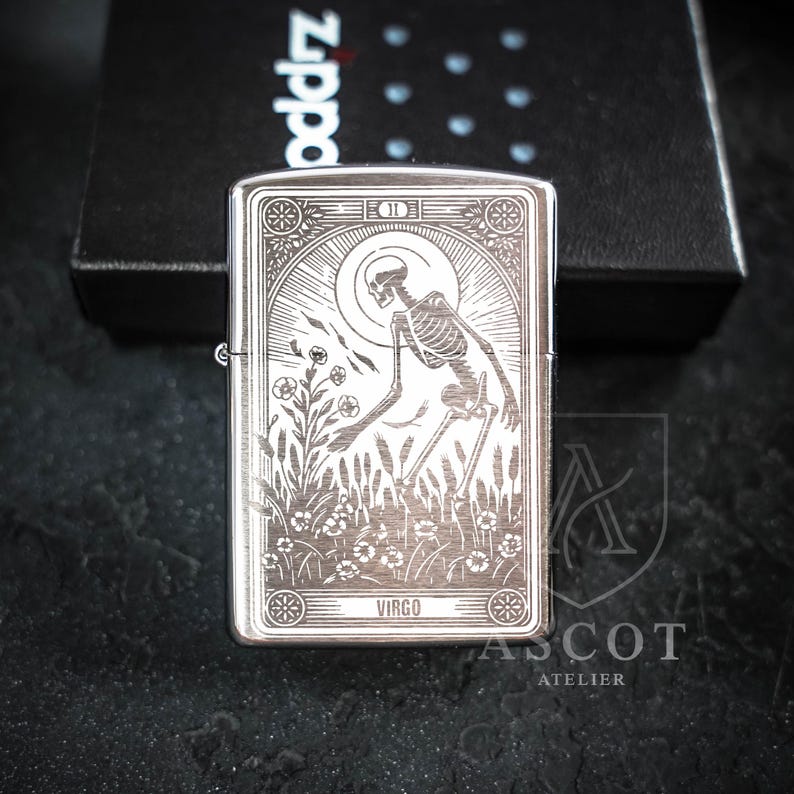 May include: A silver-toned metal lighter featuring a detailed laser-engraved design of a skeleton standing in a field of flowers under a sun motif. The engraving includes the text VIRGO at the bottom and a Roman numeral II at the top center.