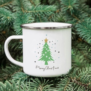 Puede incluir: Taza de esmalte blanco con un dise&ntilde;o de &aacute;rbol de Navidad verde y el texto "Merry Christmas".