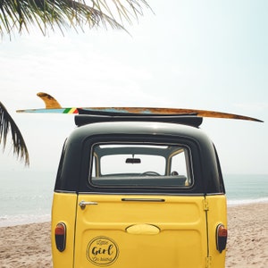 May include: A yellow vintage car with a surfboard on top. The car has a sticker on the back that says "Little Girl on Board".