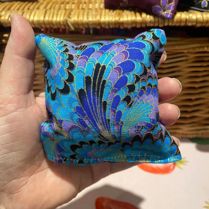 May include: A small blue and purple patterned cushion with gold accents. The cushion is made of fabric and has a soft, plush texture.