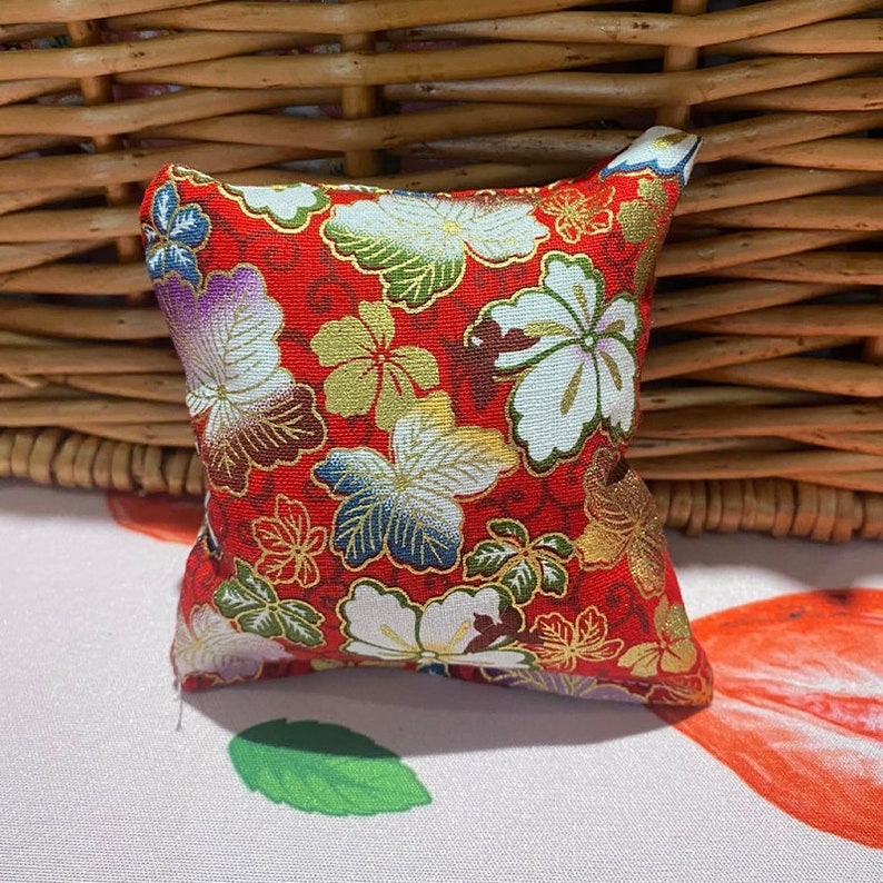 May include: A small red square cushion with a floral pattern. The cushion has white, gold, and blue flowers on a red background.