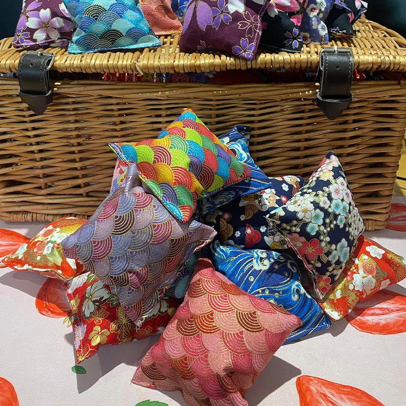 May include: A collection of colourful fabric pouches with various patterns, including floral, geometric, and wave designs. The pouches are arranged in a wicker basket and on a white surface with red accents.