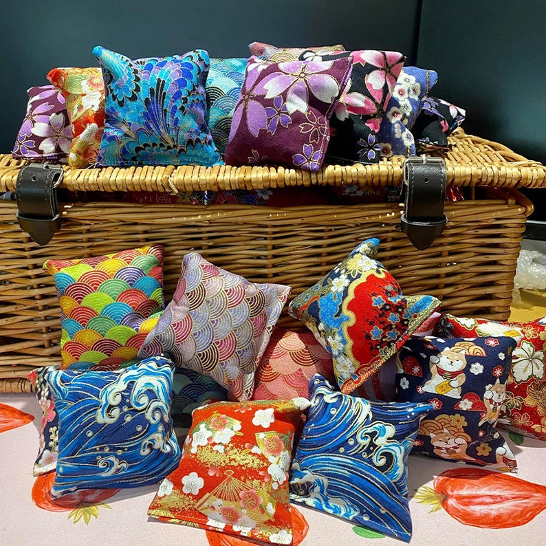May include: A wicker basket filled with colourful fabric squares featuring Japanese-inspired patterns. The squares are arranged in a variety of designs, including floral, geometric, and wave patterns. The basket is a great way to store and display these decorative squares.