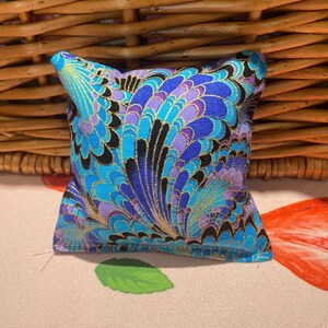 May include: A small, square cushion with a blue, purple and gold patterned fabric. The pattern features a swirling, abstract design.