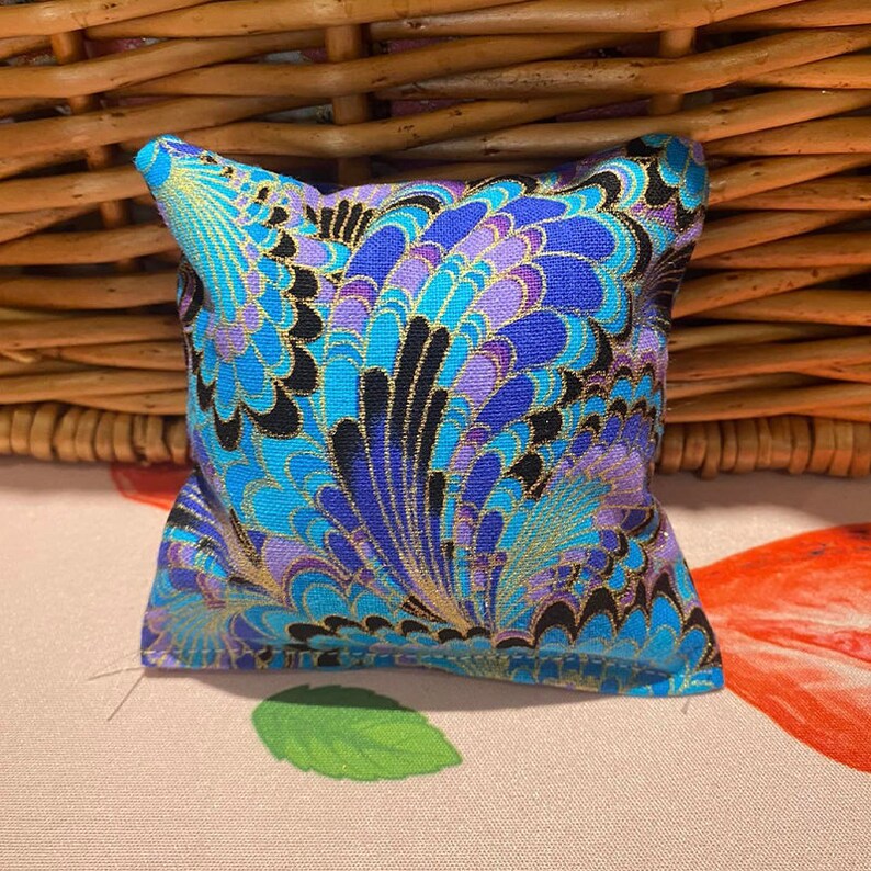 May include: A small, square cushion with a blue, purple and gold patterned fabric. The pattern features a swirling, abstract design.