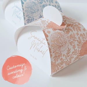 May include: Heart-shaped favor boxes in white, decorated with peach and cream floral patterns. The boxes are inscribed with "Samantha & Michael" and the date "10.12.25" in gold script. Ideal for weddings or special occasions.