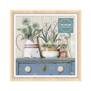 May include: A cross stitch pattern featuring a vintage blue dresser with three drawers and a keyhole.  The dresser is decorated with three white ceramic pots with flowers, including white and pink flowers. The pattern is titled "PDF Pattern CottageCoreStitches".