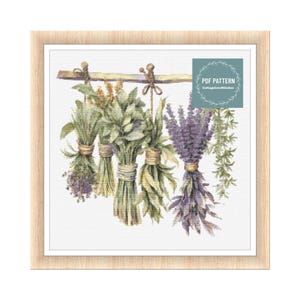 Puede incluir: Un patrón de punto de cruz con una ilustración de acuarela de una colección de hierbas secas colgadas de una barra de madera. Las hierbas incluyen lavanda, romero y otras hierbas verdes. El patrón se titula "PDF PATTERN CottageCoreStitches".