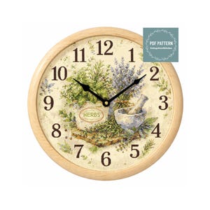 Puede incluir: Un reloj de pared redondo con marco de madera clara. La esfera del reloj presenta un diseño de punto de cruz de hierbas, un mortero y una maja, y la palabra "HERBS". Las manecillas negras indican la hora. El reloj tiene unos 25 cm de diámetro.