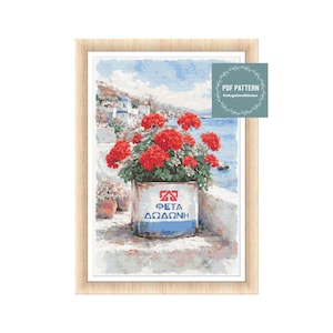 Può includere: Un modello a punto croce raffigura una scena costiera con fiori rossi in un contenitore bianco e blu. Il contenitore ha testo greco. Lo sfondo mostra mare blu, cielo e edifici bianchi. Un modello PDF è disponibile.