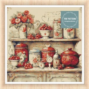 Può includere: Uno scaffale da cucina in stile vintage con barattoli, ciotole e una teiera in ceramica rossa e bianca. Lo scaffale è decorato con fiori rossi e ciliegie. Il testo "PDF PATTERN CottageCoreStitches" è nell'angolo in alto a destra dell'immagine.