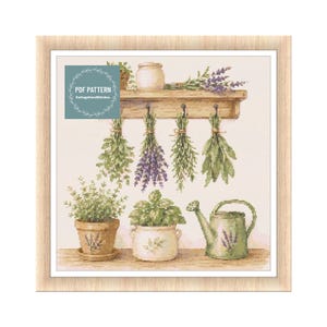 Op de afbeelding: Kruissteekpatroon met een houten plank met hangende kruiden en potplanten. Een gieter en een pot zijn ook aanwezig. De tekst "PDF PATTERN" en "CottageCoreStitches" is zichtbaar in de afbeelding.