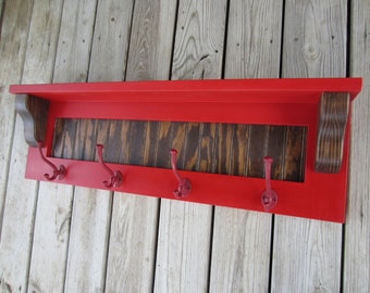 May include: Red wooden shelf with four red metal hooks and a dark wood panel in the center. The shelf is mounted on a wood wall.
