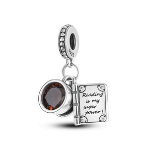 May include: Silver charm with a book and a cup with a brown gemstone. The book has the text "Reading is my super power!" on it.