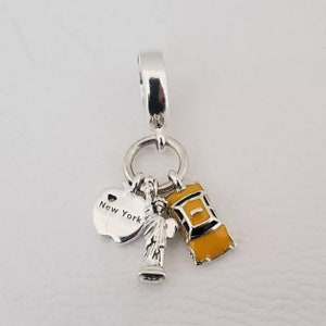 May include: Silver charm with a yellow taxi cab, a silver Statue of Liberty, and a silver apple with "New York" engraved on it.