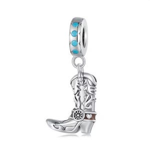 Può includere: Un charm in argento con un ciondolo a forma di stivale da cowboy. Lo stivale presenta dettagli intricati e una fascia marrone. La parte superiore del charm ha una fascia argentata con tre pietre turchesi. Un gioiello a tema western.