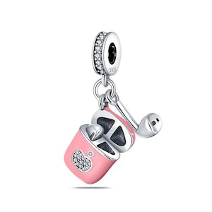 Op de afbeelding: Een zilveren bedel met een roze draadloze oortjes-etui en een enkele oortelefoon. De etui heeft een hartontwerp met heldere kristallen. De bedel bevat ook een zilveren ring met heldere kristallen rond de rand.