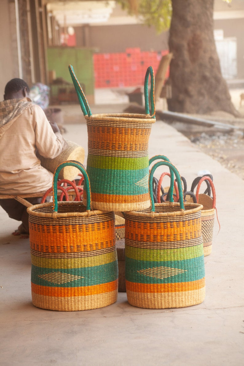 May include: Three woven baskets with handles, stacked on top of each other. The baskets are made of natural materials and have a colorful striped pattern in shades of orange, green, and brown.