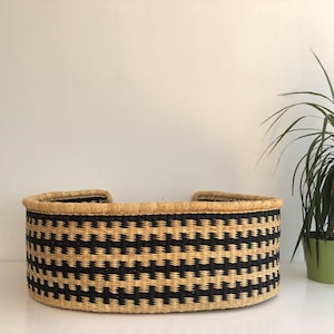 May include: A black and natural woven pet bed with a rounded shape. The bed is made of natural materials and has a black and natural woven pattern.