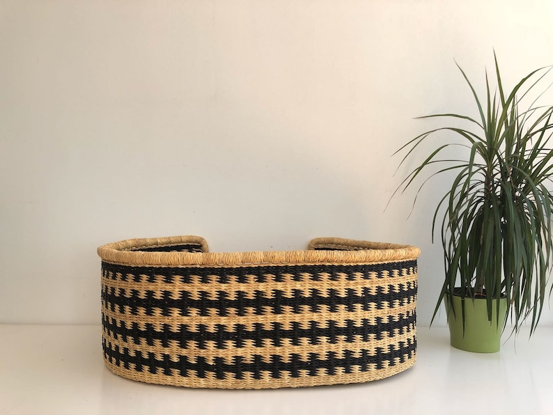May include: A black and natural woven pet bed with a rounded shape. The bed is made of natural materials and has a black and natural woven pattern.