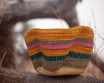 May include: A woven basket with a colorful striped pattern in shades of yellow, orange, pink, teal, and brown. The basket is made of natural fibers and has a rounded shape.