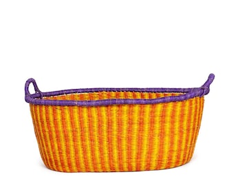 May include: A large, oval-shaped storage basket woven from natural materials. The basket has a yellow and orange striped pattern with a purple trim around the top and handles.