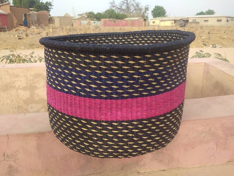 May include: A woven basket with a black rim and a curved top. The basket features a pattern of black, blue, and tan woven fibers, with a vibrant pink stripe. The basket is likely used for storage or decoration.