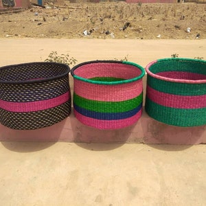 May include: Three woven baskets in a row. The baskets are cylindrical with colorful horizontal stripes. The first basket is black with a pink stripe. The second basket is pink, green, and blue. The third basket is green and pink.