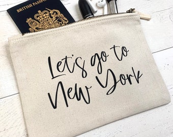 May include: A beige canvas zippered pouch with the text "Let's go to New York" printed in black. The pouch is partially open and a British passport is visible inside.