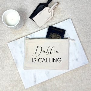 May include: A white canvas zippered pouch with the text "Dublin is Calling" in black lettering. A passport is partially visible inside the pouch.