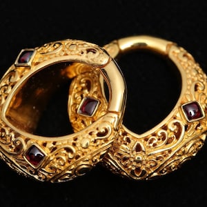 May include: A pair of gold hoop earrings with intricate filigree designs and red gemstone accents.