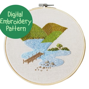 May include: Digital embroidery pattern for a landscape scene with green hills, a blue lake, a small island with a tree, and a wooden dock. The pattern is displayed in a wooden embroidery hoop.