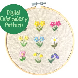 Op de afbeelding: Een digitaal borduurpatroon met een verscheidenheid aan kleurrijke, geborduurde bloemen. De bloemen omvatten gele, roze, blauwe en witte bloesems, elk met groene stelen en bladeren. Het ontwerp wordt weergegeven op een beige stof in een houten borduurring. De tekst "Digital Embroidery Pattern" staat in een groene cirkel.