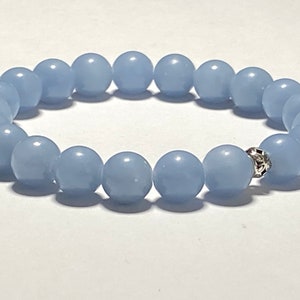 May include: A light blue beaded bracelet. The bracelet features round, smooth beads in a soft, pastel blue color. A decorative silver-colored bead is visible. The bracelet is likely made of a stretch cord.