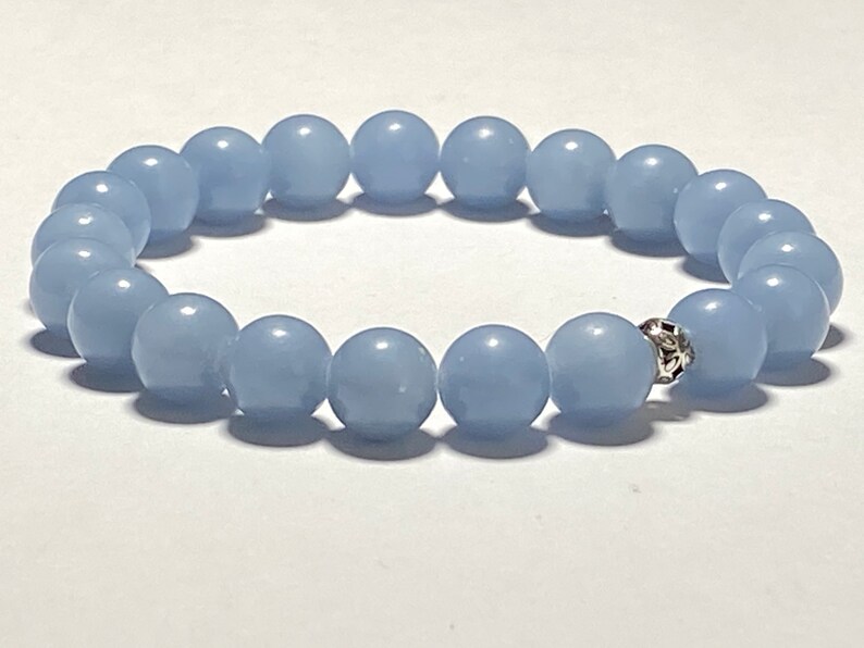 May include: A light blue beaded bracelet. The bracelet features round, smooth beads in a soft, pastel blue color. A decorative silver-colored bead is visible. The bracelet is likely made of a stretch cord.