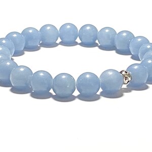 May include: A light blue beaded bracelet. The bracelet features round, polished beads in a soft, pastel blue color. A silver-colored accent piece is visible. The beads are strung together to form a complete circle. The bracelet is displayed on a white background.