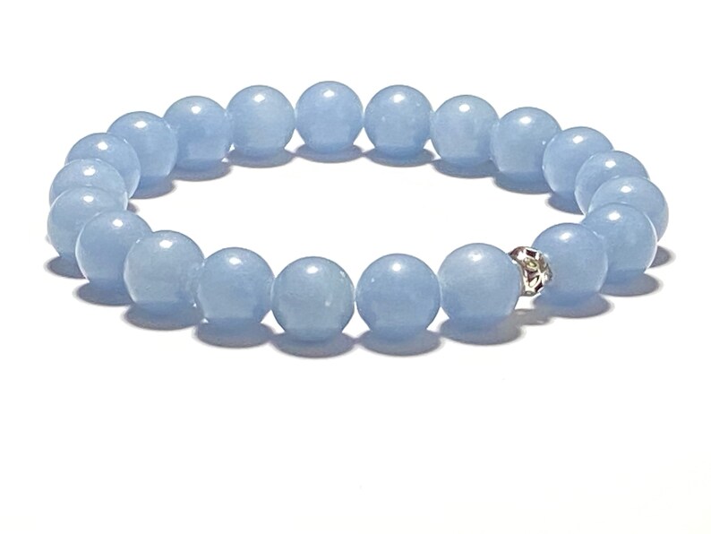 May include: A light blue beaded bracelet. The bracelet features round, polished beads in a soft, pastel blue color. A silver-colored accent piece is visible. The beads are strung together to form a complete circle. The bracelet is displayed on a white background.