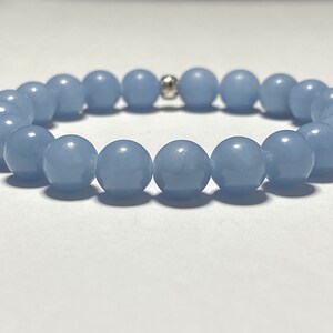 May include: A light blue beaded bracelet. The bracelet features round, smooth beads strung together with a silver-colored accent bead. The beads are a soft, pastel blue color, and the bracelet is displayed on a white surface.