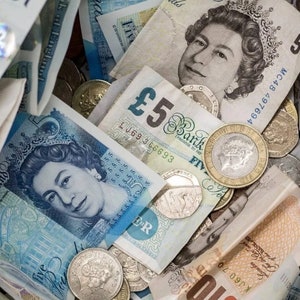 May include: A close-up of a pile of British currency, including five pound notes and coins. The notes feature a portrait of Queen Elizabeth II and the text "£5 Bank of England Promise to Pay Five Pounds".