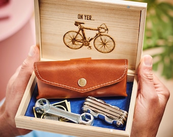 May include: A wooden box with a leather pouch and a multi-tool inside. The box has a laser-engraved image of a bicycle with the text "On Yer..." on the lid.