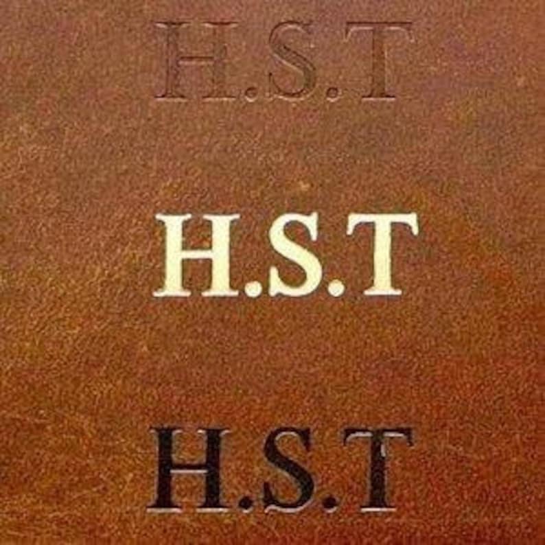 May include: Close-up of a brown leather surface with the initials "H.S.T." embossed in three different styles: debossed, white, and black. The leather has a textured appearance.