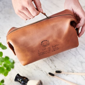 May include: A brown leather toiletry bag with a zipper closure. The bag has a personalized message that says "I love my dada because he has a wonderful smile" with a simple drawing of a person.